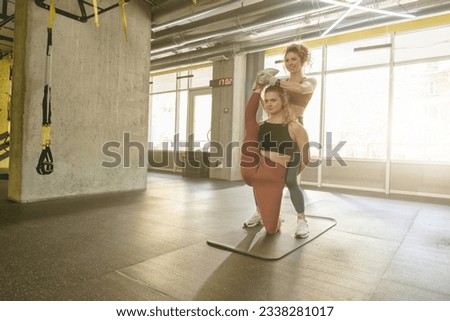 Athletic young woman doing stretching exercises with the help of personal trainer at gym