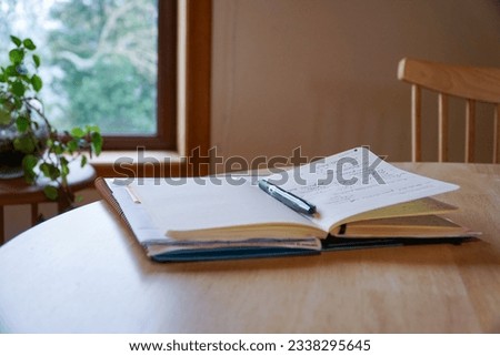 An open notebook with a pencil placed on top, resting on a wooden table inside the house, symbolizing creativity and ideas in a cozy home setting. Royalty-Free Stock Photo #2338295645