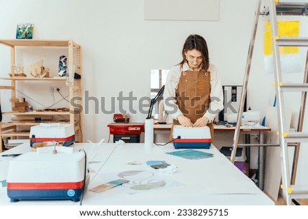 Angle view portrait of a female working with piece of mirror glass using glass grinding machine. Hobbies, arts and crafts concept. Artist creating in art studio with stained glass windows.