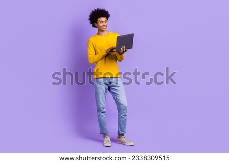 Full size photo of pleasant friendly guy dressed yellow long sleeve denim pants typing email on laptop isolated on purple color background