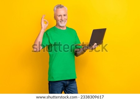 Photo of handsome aged man toothy smile hold wireless netbook demonstrate okey symbol isolated on yellow color background