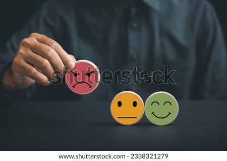 Unsatisfied customer holding frown icon on wooden circle. Conceptual representation of customer satisfaction evaluation, depicting bad experience, negative review, and low score. Royalty-Free Stock Photo #2338321279