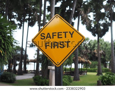 The yellow label has black text in the frame that says "Safety first" installed on steel poles within the park. Safety symbols on sky and tree background. Remind us the importance of safety.