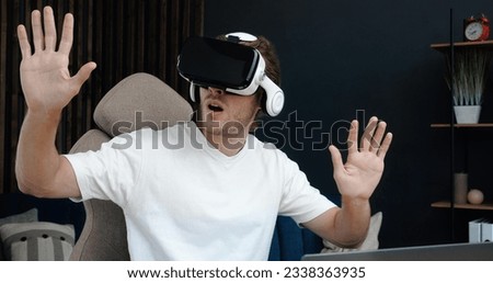 Portrait of Handsome Caucasian man in white t-shirt is sitting at Home Office wearing VR glasses. Young Caucasian Freelancer, enjoying VR glasses while sitting at his desk.
