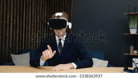 Portrait of Handsome Caucasian Businessman in Suit is sitting at Home Office wearing VR glasses. Young Caucasian Freelancer, Couch, Call-Center Worker, Mentor, Lector online is enjoying VR glasses Royalty-Free Stock Photo #2338363937