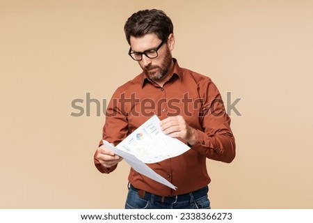 Pensive, serious, businessman wearing glasses holding business graph isolated on beige background. Male teacher working with documents Royalty-Free Stock Photo #2338366273