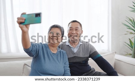 Happy elderly asian couple taking selfie looking at smartphone, Cheerful asian grandparents having fun holding phone make snapshot selfie. Old couple taking selfie on cellphone