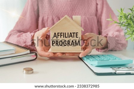 Affiliate Program text on a miniature of a wooden house in the hands of a woman at the office table Royalty-Free Stock Photo #2338372985