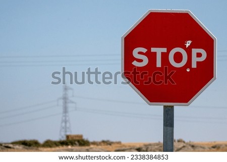 Stop sign, which has been shot with a firearm, in the background you can see cables and an electric tower. Concept: prohibited, demand power station Royalty-Free Stock Photo #2338384853