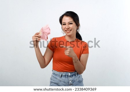 Smiling beautiful Asian woman wearing casual shirt holding Indonesian money isolated on white background