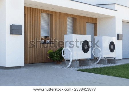 A pair of air source heat pumps, an eco-friendly home heating solution, installed at a contemporary residential property. Royalty-Free Stock Photo #2338413899