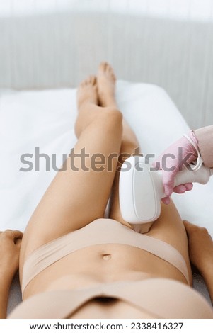 Anonymous beautician in gloves using laser hair removal apparatus on bikini zone of female client during beauty laser skin care procedure on stomach in modern salon. Laser epilation at beauty clinic.