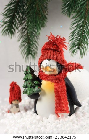 Cute smiling penguin with red scarf and hat, holding a Christmas tree in its hand, standing in the snow.Beautiful composition for winter background.