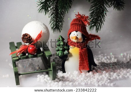 Cute smiling penguin with red scarf and hat, holding a Christmas tree in its hand, standing in the snow.Beautiful composition for winter background.