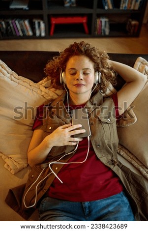 Young woman using a smart phone and listening to music on the couch in the living room