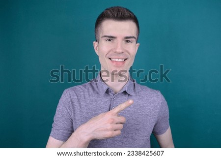 Happy Young Handsome Man Pointing Sideways - Indicating Direction or Interest on Blue Background