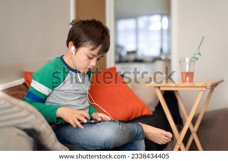 Kid wearing headset listening to music,Young sitting on sofa watching cartoons or playing games on tablet,Child boy using digital pad learning lesson on internet, Learning online education concept
