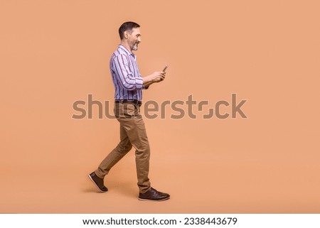 Full size profile photo of handsome positive man walking use smart phone empty space ad isolated on beige color background