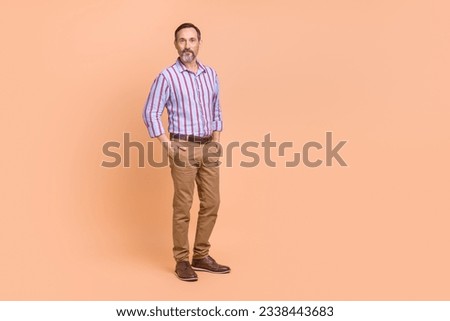 Photo of good mood handsome man with white gray beard wear striped shirt standing arms in pockets isolated on beige color background