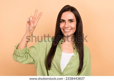 Photo of nice positive young lady beaming smile arm fingers demonstrate v-sign isolated on beige color background