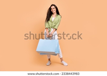 Full length photo of pretty woman wear green shirt look at promotion empty space hold shopping bags isolated on beige color background