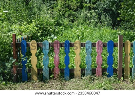 Colorful wooden fence near the green garden. Grass with trees in the garden
