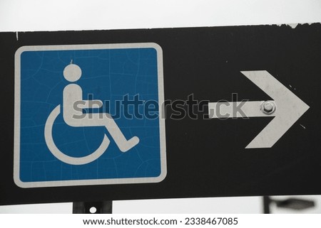 handicap sign blue logo with white arrow on its right pointing right on black rectangle horizontal sign on post with sky in background