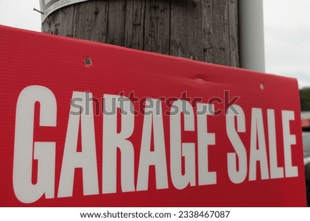 garage sale sign in white capital letters on red background fastened to wood post with sky in background, shot on angle