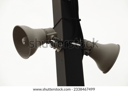 two beige train station speakers pointing in opposite directions fastened to a black rectangular post outside at train station with sky in background Royalty-Free Stock Photo #2338467499