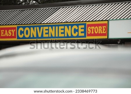 easy convenience store front entrance sign with blurred hood of car in foreground, red yellow blue sign with roof above it