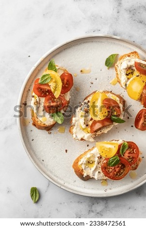 Bruschetta sandwiches with tomatoes, cream cheese, olive oil and basil on a plate on white marble background, top view. Traditional italian antipasti. Vertical Royalty-Free Stock Photo #2338472561