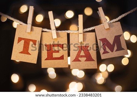 The word TEAM printed on clothespin clipped cards in front of defocused glowing lights.