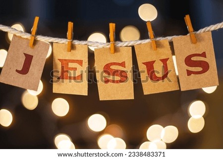 The name JESUS printed on clothespin clipped cards in front of defocused glowing lights.