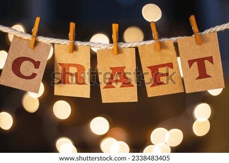 The word CRAFT printed on clothespin clipped cards in front of defocused glowing lights.