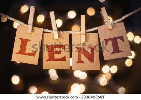 The word LENT printed on clothespin clipped cards in front of defocused glowing lights.