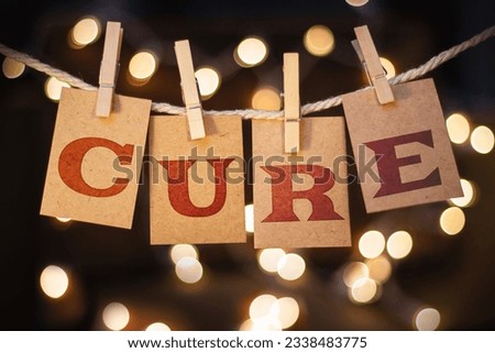 The word CURE spelled out on clothespin clipped cards in front of glowing lights.