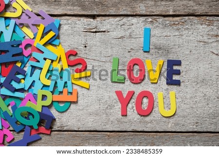 The colorful words -I LOVE YOU- made with wooden letters next to a pile of other letters over old wooden board.