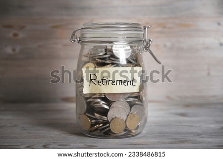 Coins in glass jar with retirement label, financial concept. Vintage wooden background with dramatic light.