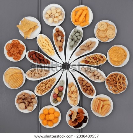 Large savoury snack selection in porcelain dishes over grey wooden background.