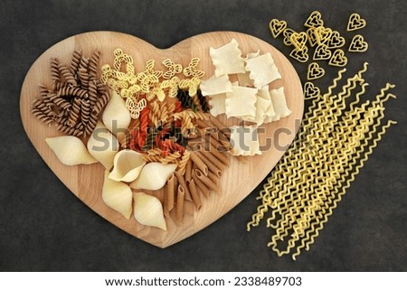 Dried pasta food selection on a heart shaped wooden board.
