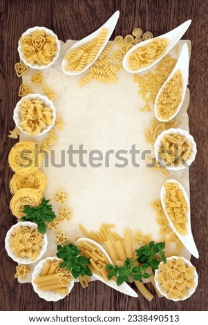 Italian pasta selection and basil herb forming an abstract border over old parchment and oak background.