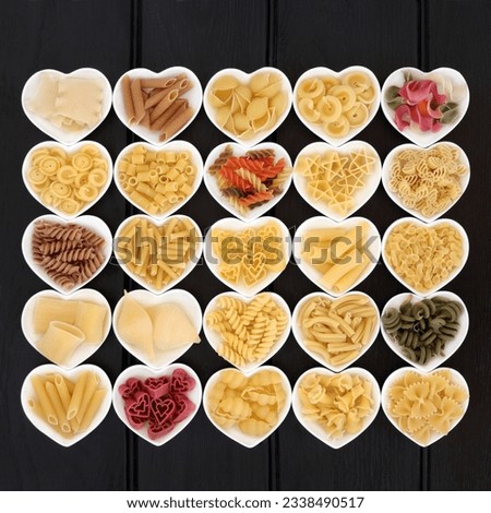 Pasta dried food selection in heart shaped porcelain dishes over dark wood background.