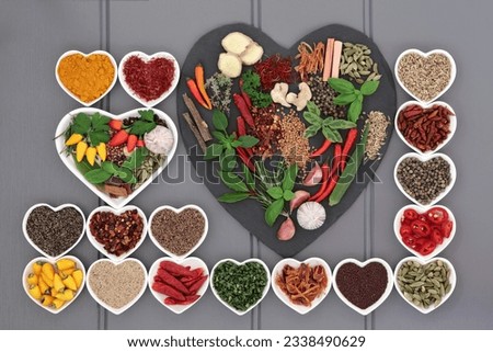 Herb and spice ingredients on a heart shaped slate and in porcelain dishes over wooden grey background.