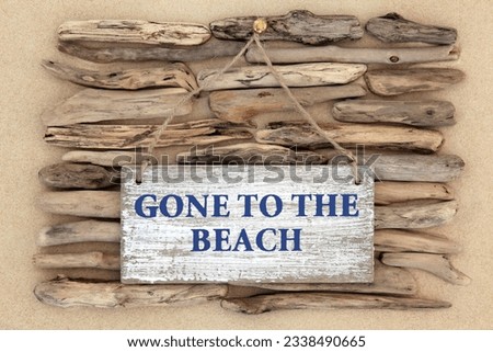 Gone to the beach weathered sign on driftwood and sand background.