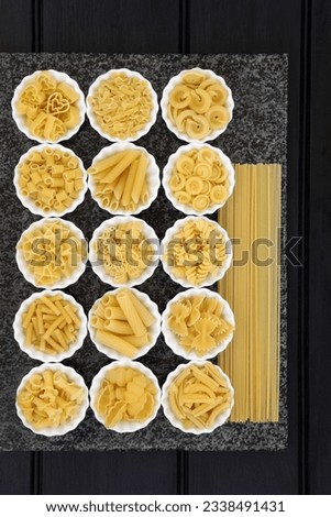Pasta spaghetti dried food selection in porcelain crinkle bowls on a marble slab over dark wood background.