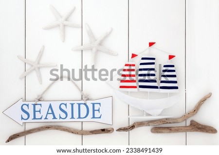 Seaside sign, starfish shells, driftwood and decorative sailing boat over wooden white background.
