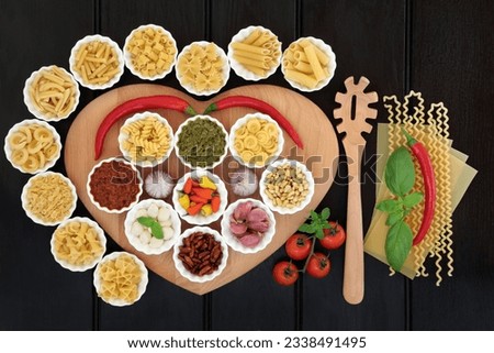 Italian pasta and mediterranean food ingredients on a heart shaped board in porcelain bowls over dark wood background.
