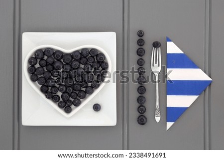 Blueberry fruit in a heart shaped dish with a striped napkin and old silver fork.