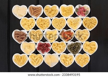 Italian pasta dried food selection in heart shaped porcelain dishes over dark wood background.