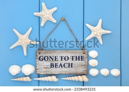 Gone to the beach sign with starfish, cockle and turritella seashells over wooden blue background.